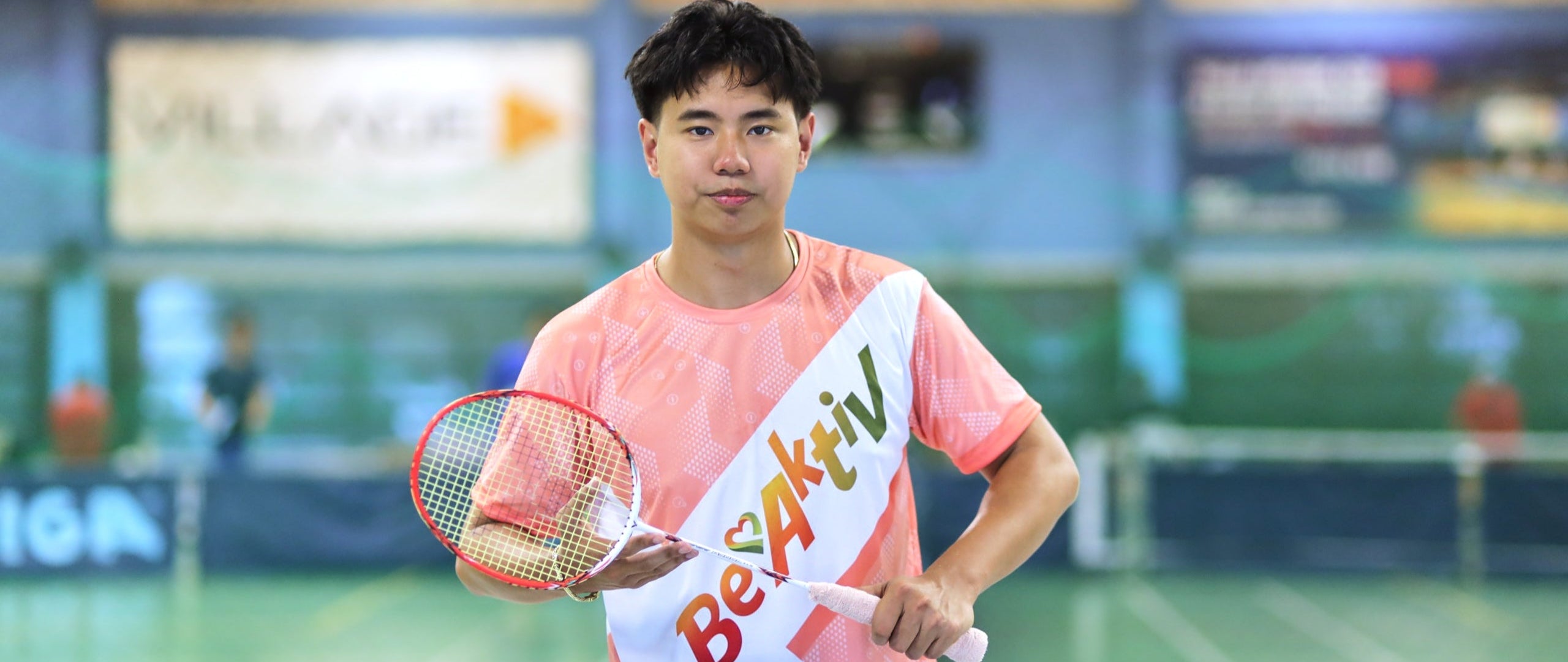 Person holding a badminton racket with a brand banner on a badminton court
